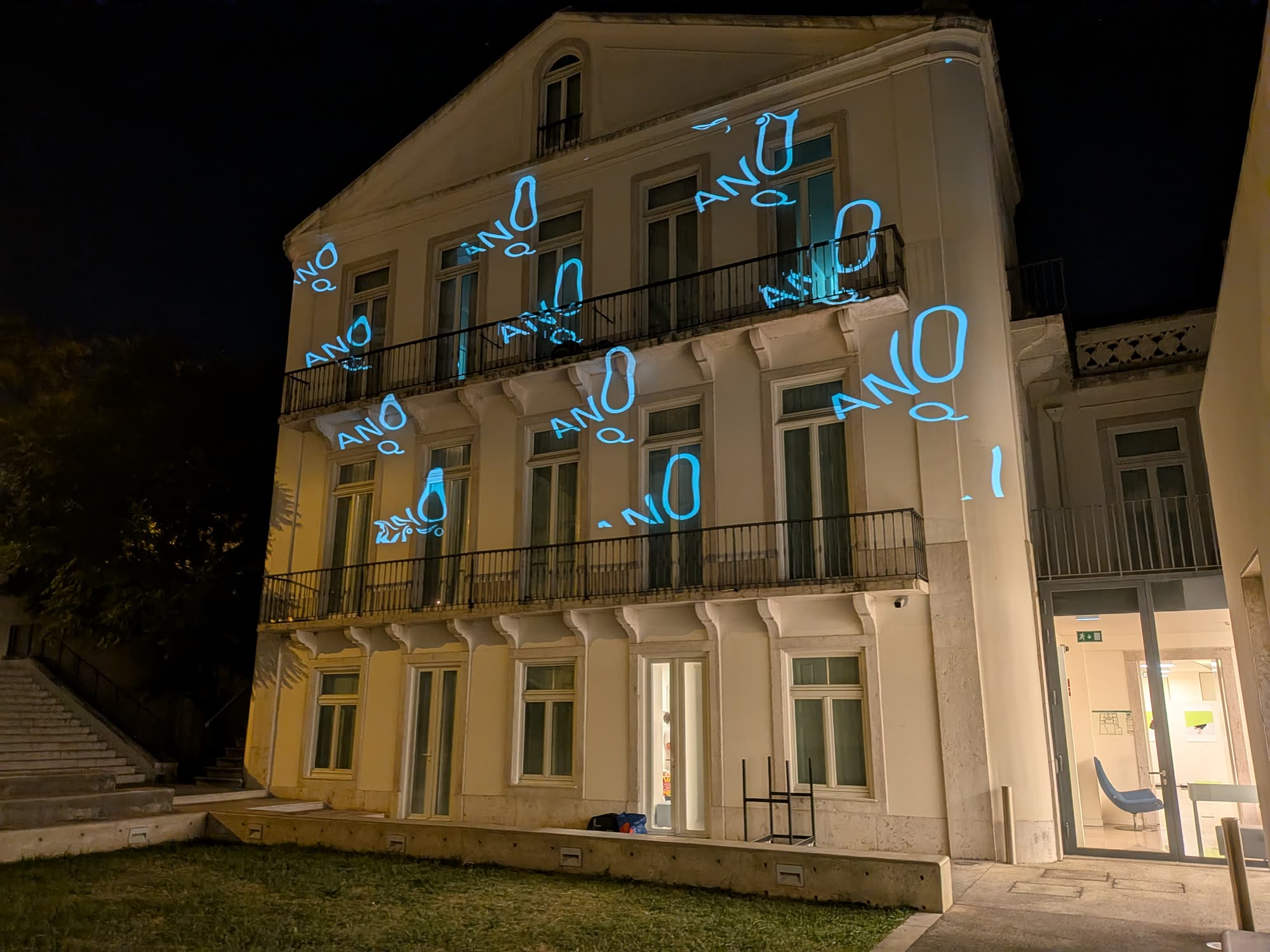 Blue ANO Q lettering projected across the facade of a three-storey building at night