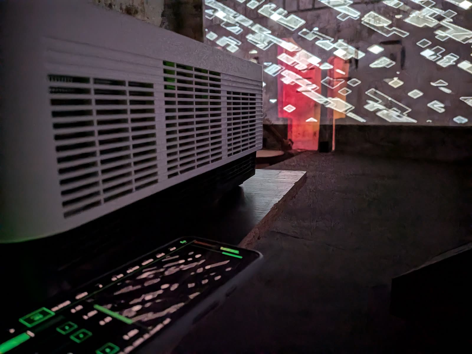 PVJ controls glowing green on a phone next to a projector throwing white shapes on a stone wall